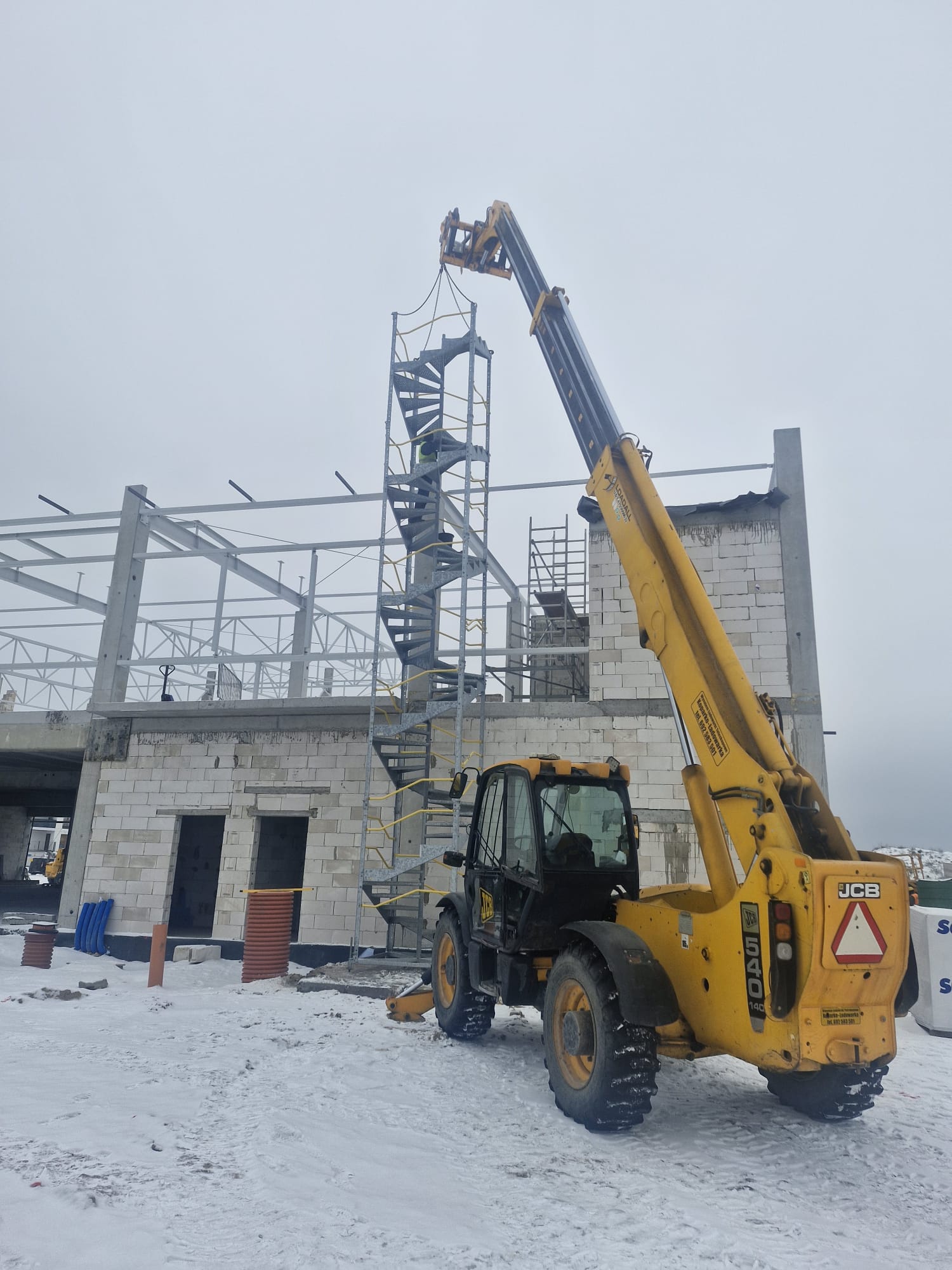 Transport materiałów na dach budynku ładowarką teleskopową